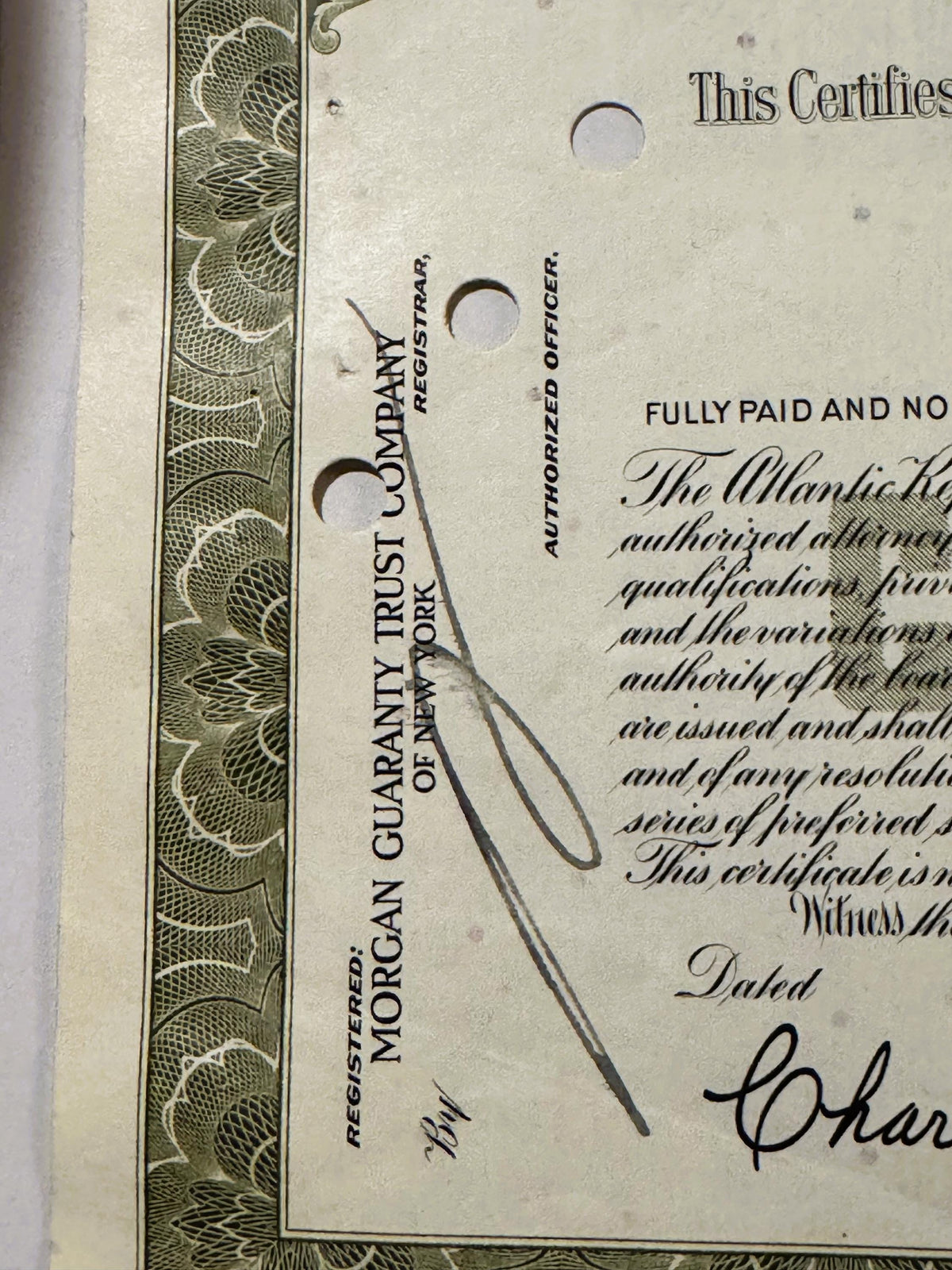 Close-up of vintage stock certificate with ornate border, showing "Morgan Guaranty Trust Company" text, punch holes, handwrit