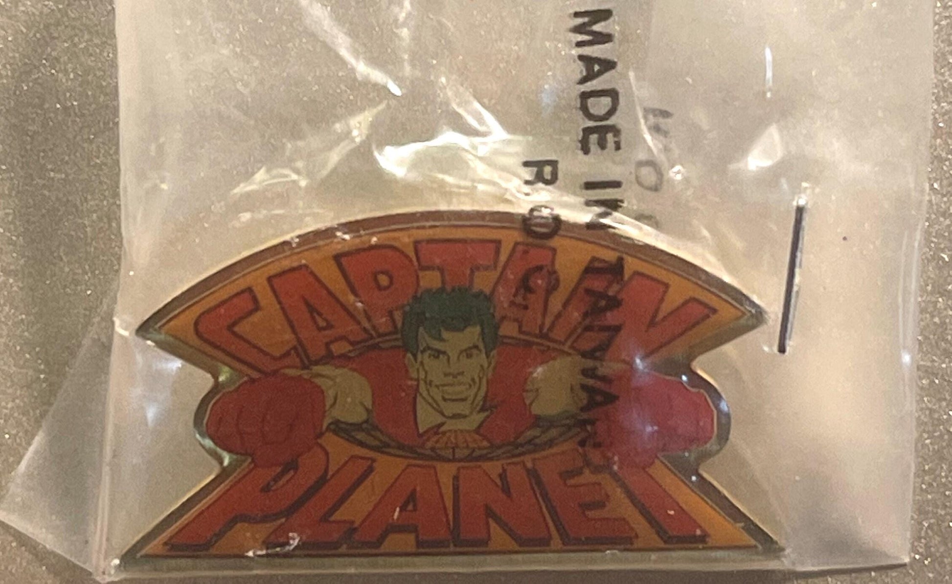 Vintage Captain Planet enamel pin in original sealed plastic bag, showing red logo with illustrated character face, made in T
