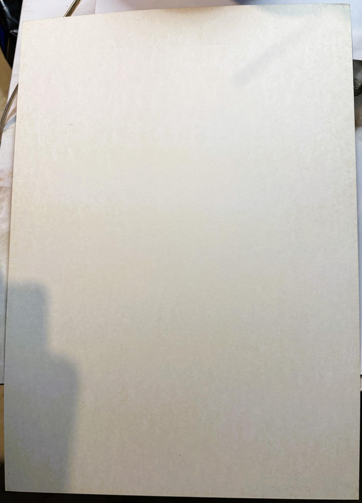 Blank cream-colored poster board lying flat on a surface, photographed from above with shadow visible on left side