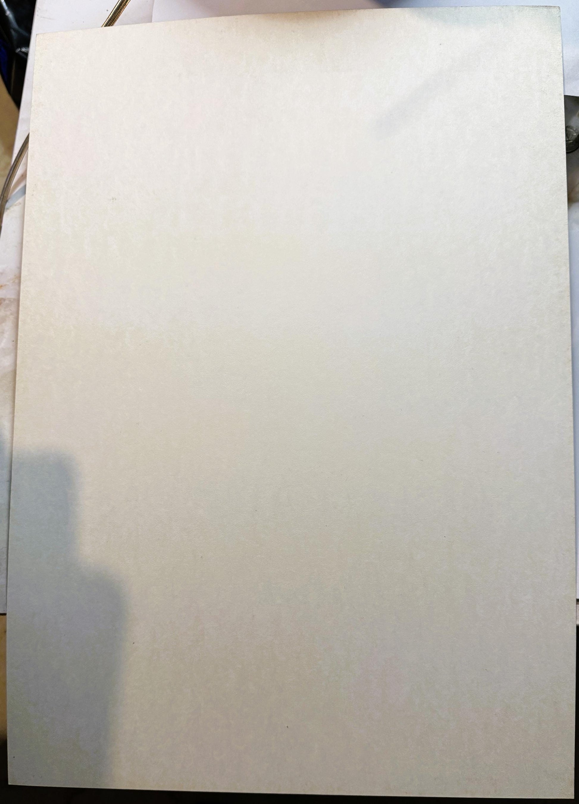 Blank cream-colored poster board lying flat on a surface, photographed from above with shadow visible on left side