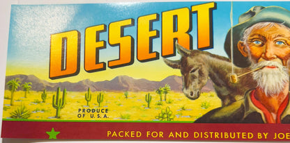 Vintage fruit crate label featuring "Desert" in large yellow letters, bearded prospector with donkey in desert landscape with