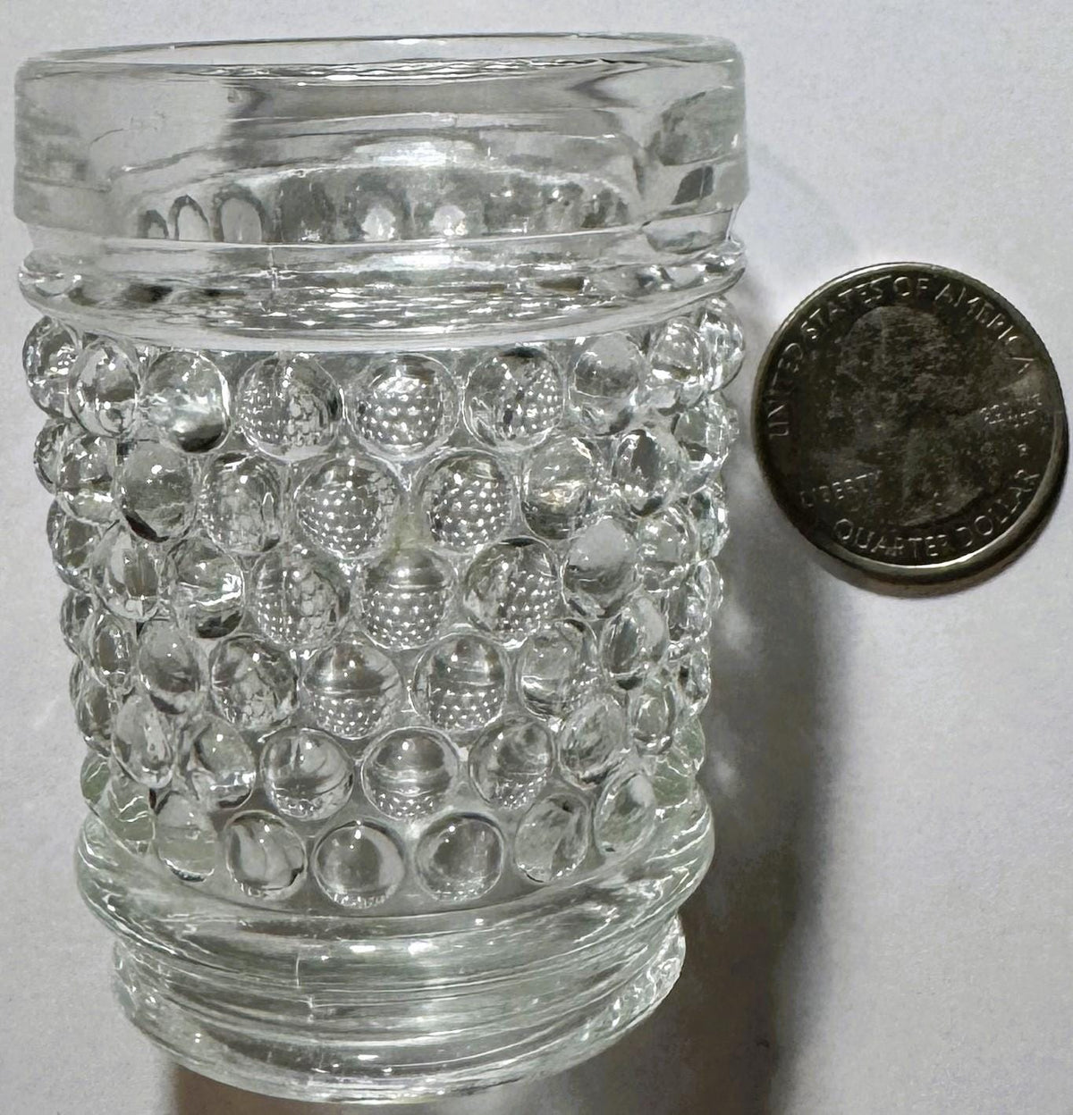 Clear hobnail glass tumbler next to a quarter coin for scale, showing textured bubble pattern and flat base