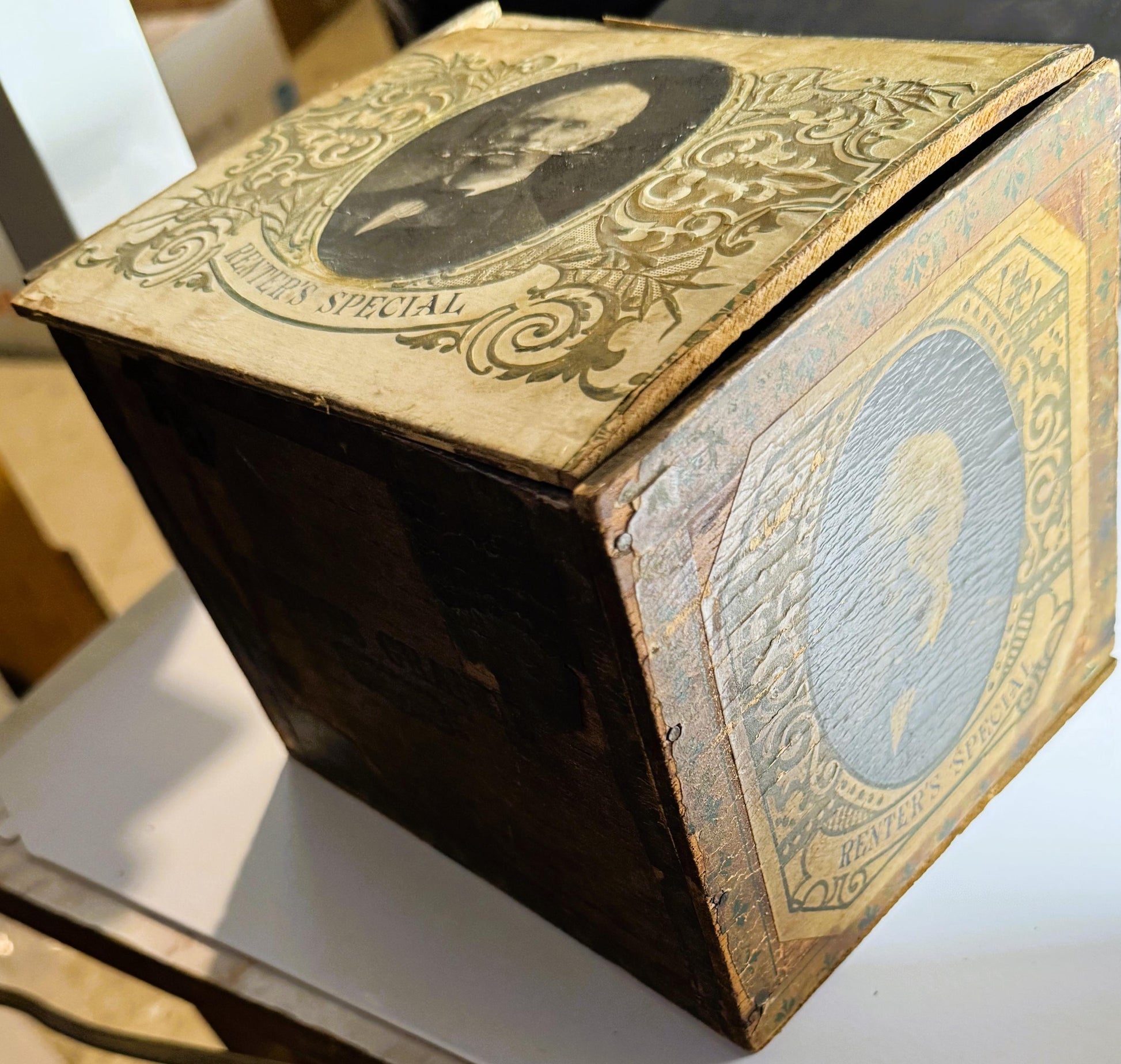 Antique wooden cigar box with ornate gold embossing and portrait medallion, displayed at angle showing top and side panels wi