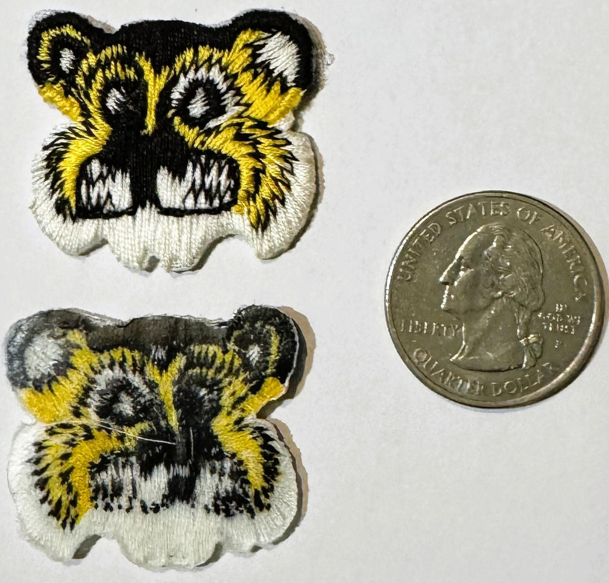 Two embroidered tiger face patches in yellow, black and white next to a US quarter dollar coin for scale.
