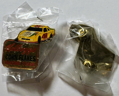Two vintage NASCAR pins in clear plastic bags on white surface: yellow and red race car pin with "Corn Flakes" text, and bron
