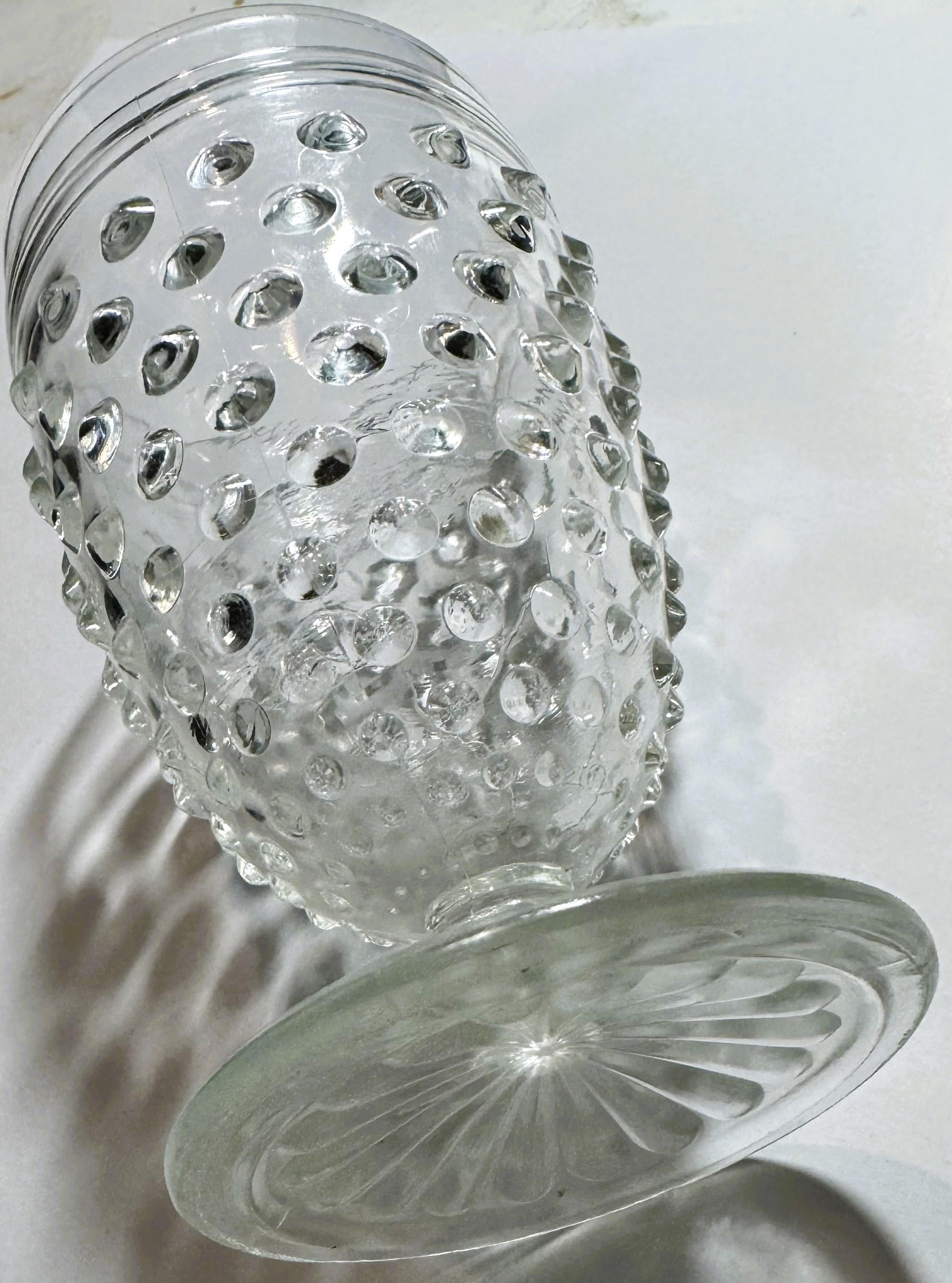 Clear glass hobnail tumbler and matching saucer with dimpled texture, photographed at an angle against white background showi