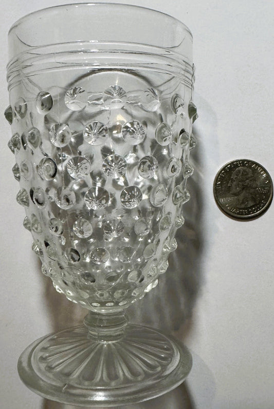 Clear footed hobnail juice glass standing beside a U.S. quarter for scale