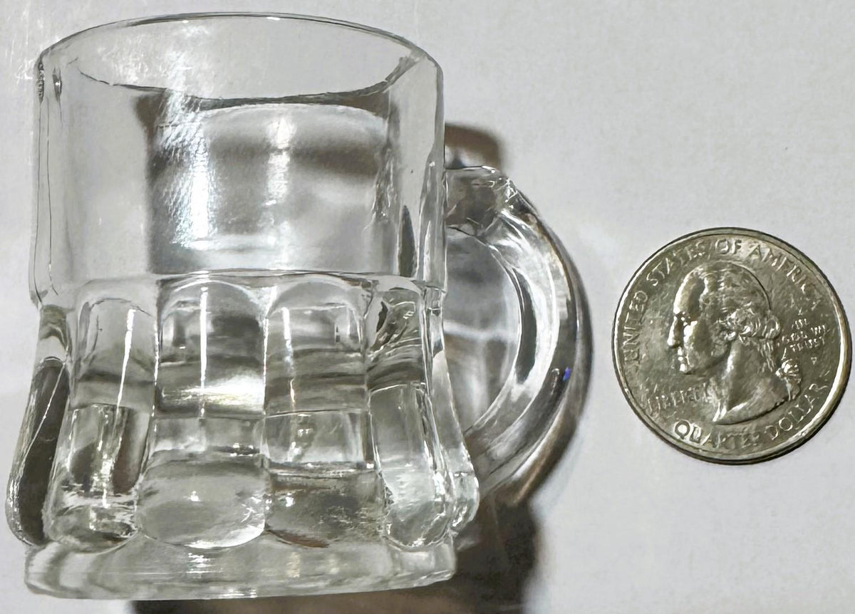 Clear hobnail glass shot or juice glass next to a quarter for scale, showing textured dimpled pattern and handle detail.