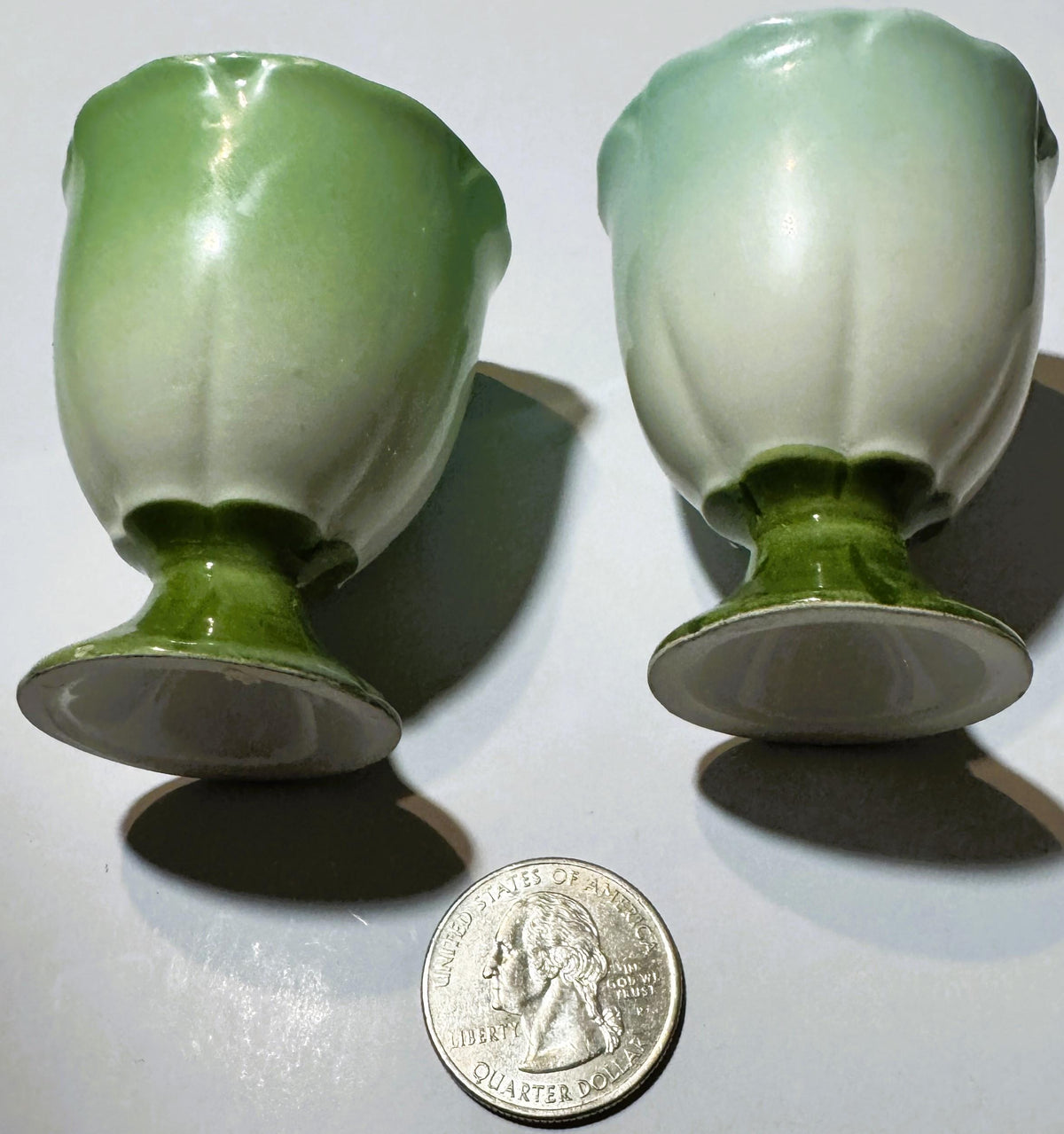 Two vintage mid-century ceramic egg cups in green and white glaze, shown from front angle with a US quarter coin placed below for scale.