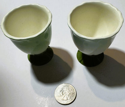 Two vintage ceramic egg cups with cream interiors and green exteriors, pedestal bases, shown with a U.S. quarter for scale against white background.