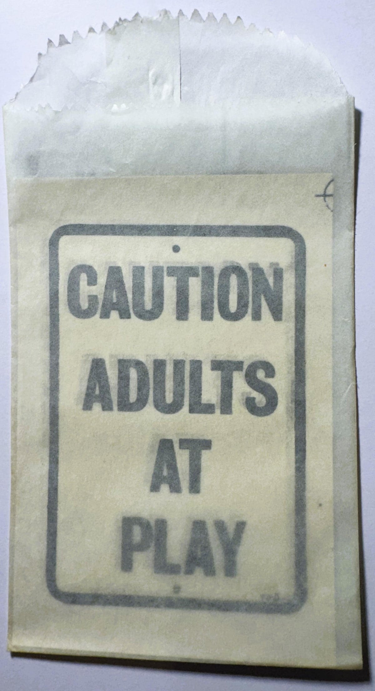 Vintage paper packet with "CAUTION ADULTS AT PLAY" printed text, shown against white background with crinkled top edge