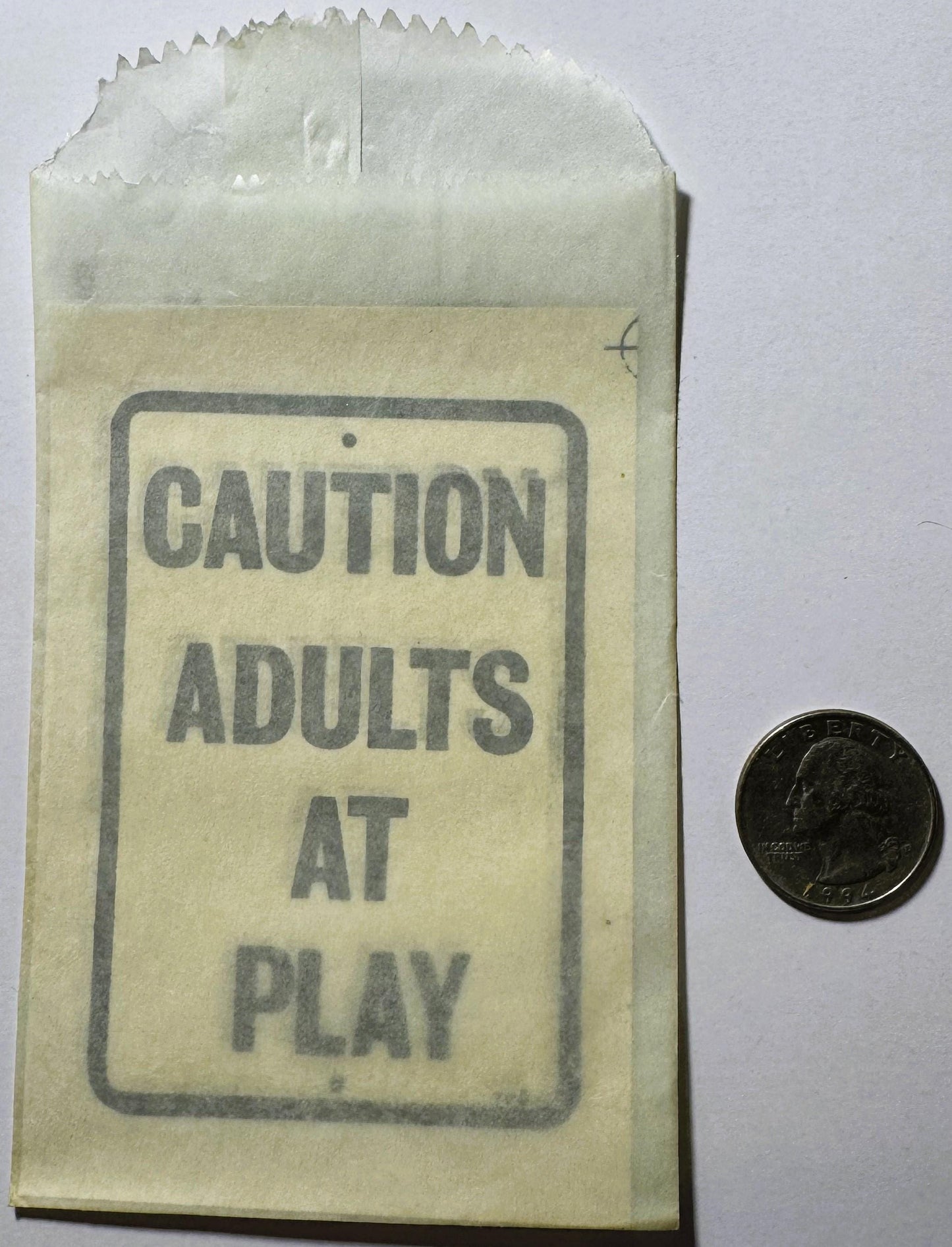 Vintage paper envelope with "CAUTION ADULTS AT PLAY" printed text, displayed next to a quarter for scale
