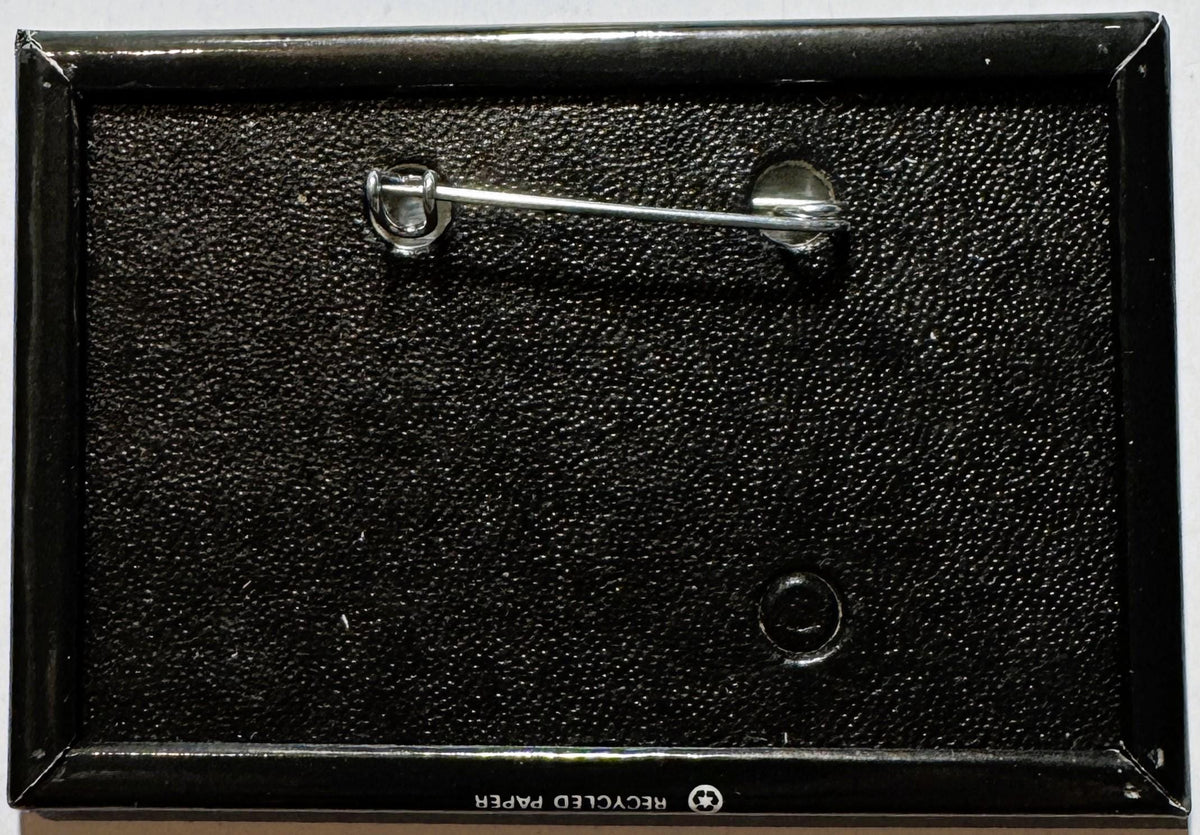 Vintage enamel pin in black packaging with metal clasp, shown from above against textured background