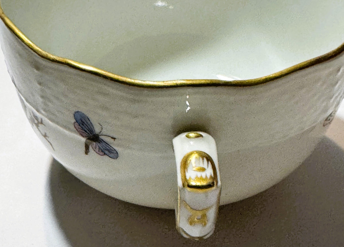 Close-up of Herend porcelain teacup interior showing hand-painted dragonfly, gilt rim, and handle with gold accents against w