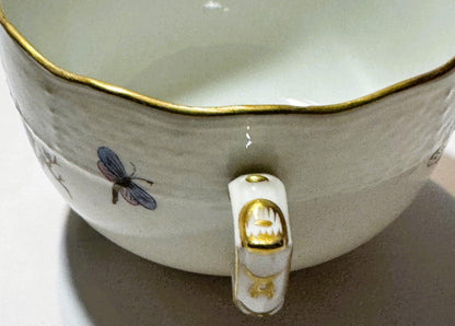 Close-up of Herend porcelain teacup interior showing hand-painted dragonfly, gilt rim, and handle with gold accents against w