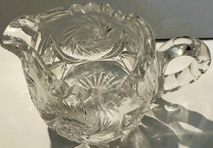 Clear glass creamer with pinwheel and hobstar cut patterns, photographed from above against white background with hand visibl