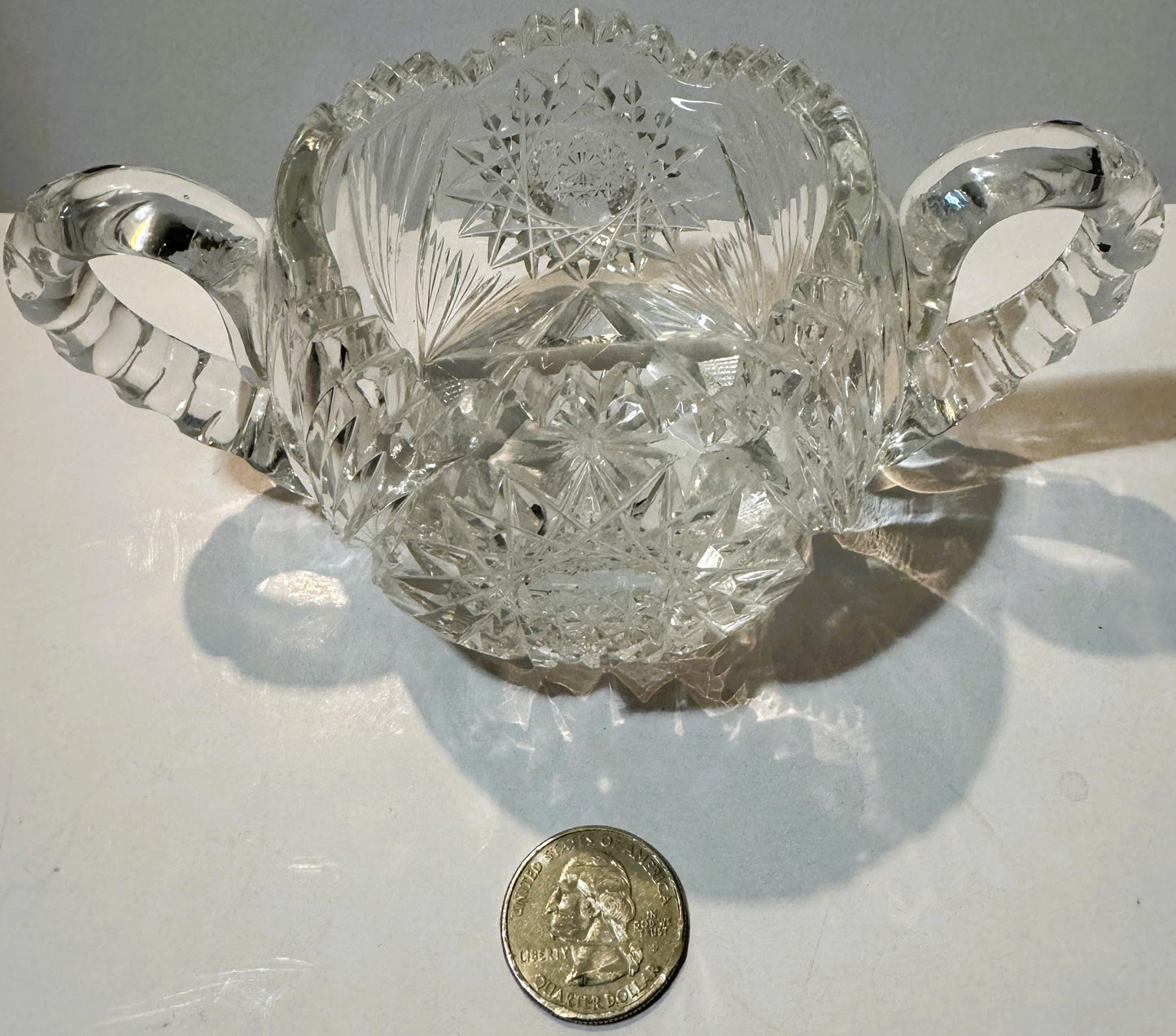 Antique cut glass two-handled sugar bowl with geometric patterns, displayed with a quarter dollar for scale