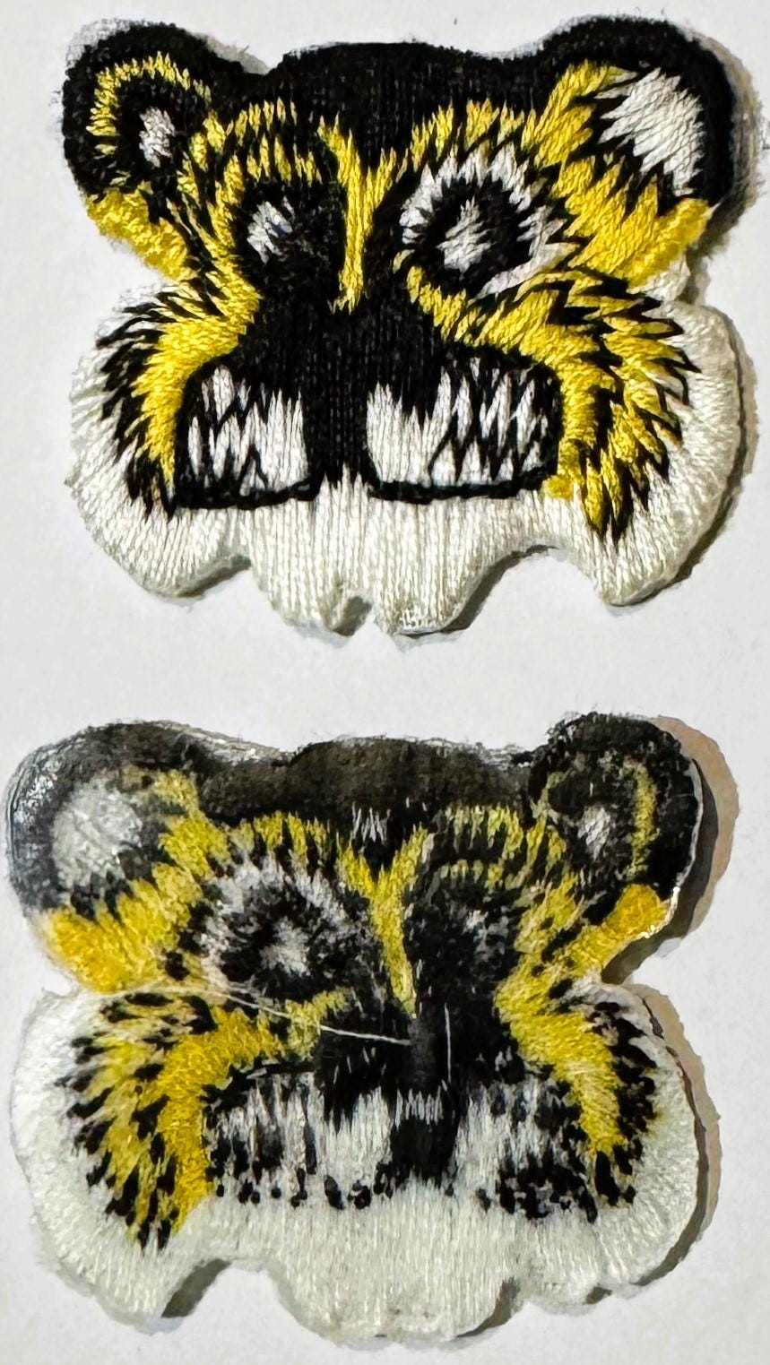 Two embroidered tiger face patches shown front and angled view, yellow black and white thread on cream background, approximat