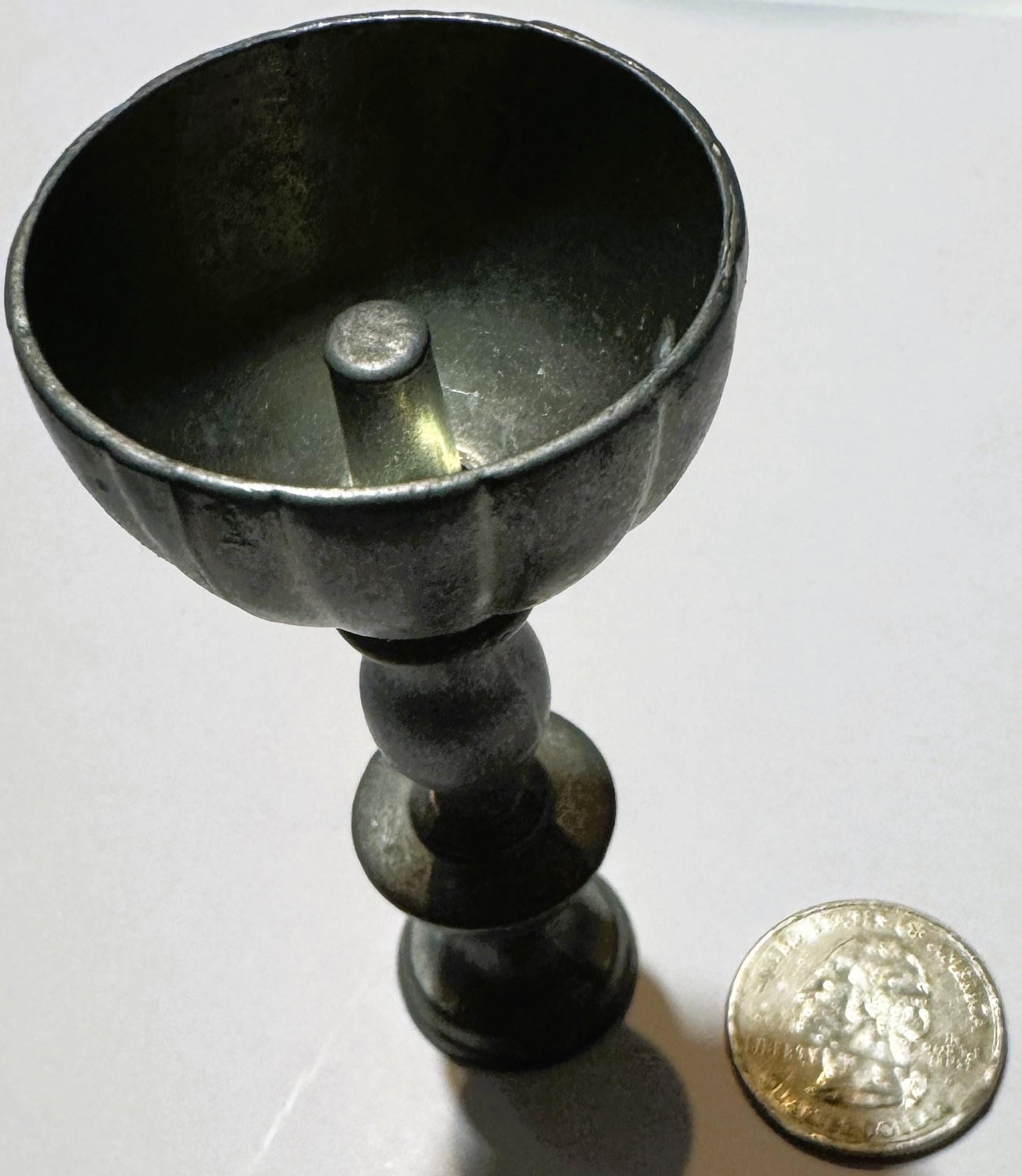 Miniature pewter goblet with fluted bowl and baluster stem next to a quarter for scale, showing patina and maker's stamp on b