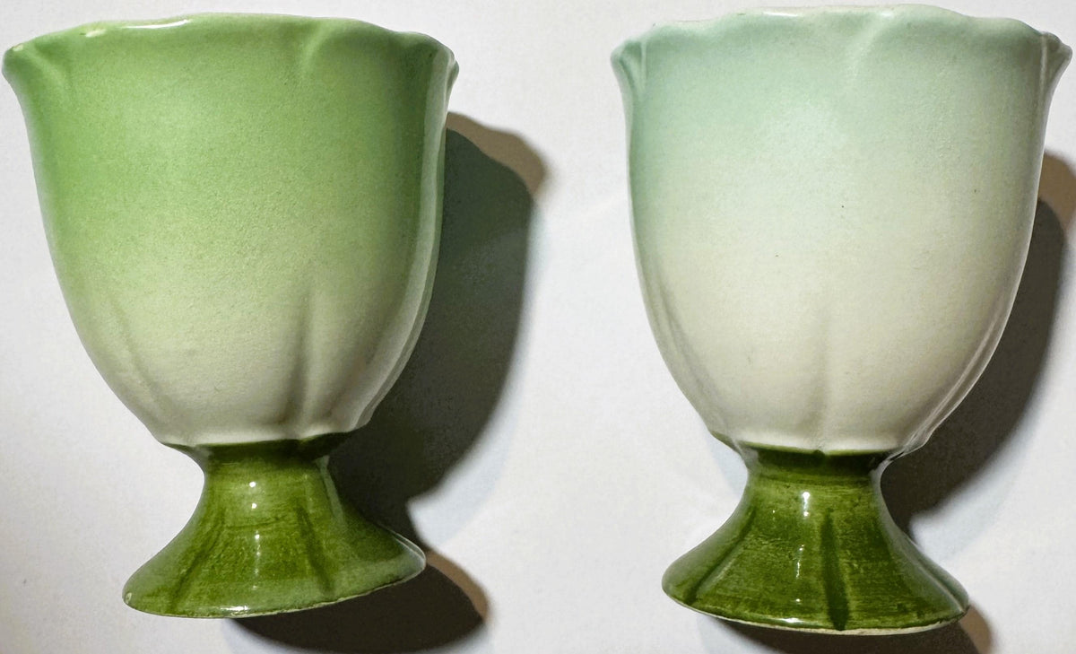 Two vintage ceramic egg cups with pale green tulip-shaped bowls on darker green pedestal bases, shown from front view against white background.