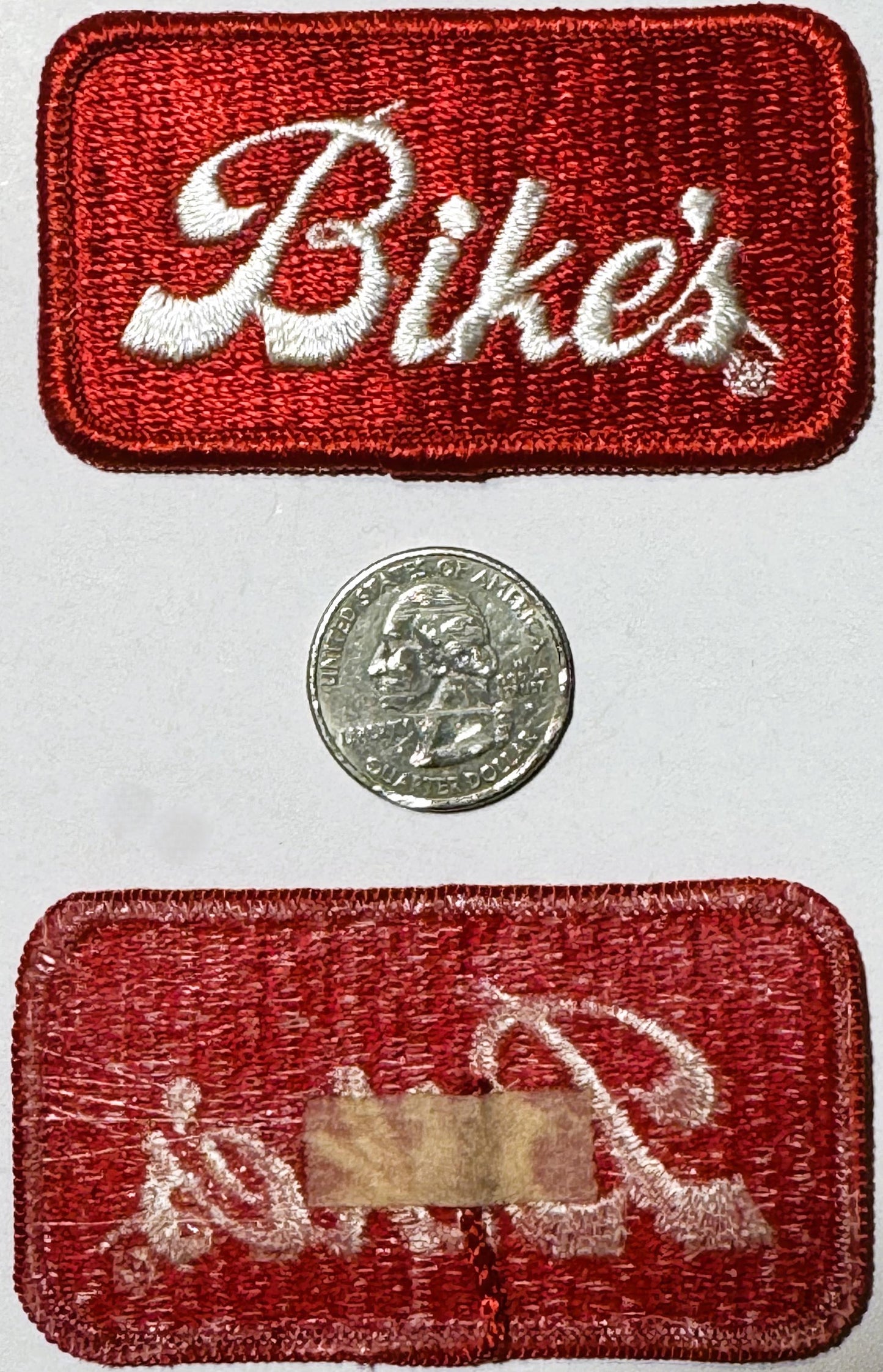 Red embroidered patch with white cursive "Biker" text and small diamond, displayed with quarter coin for scale and reverse si
