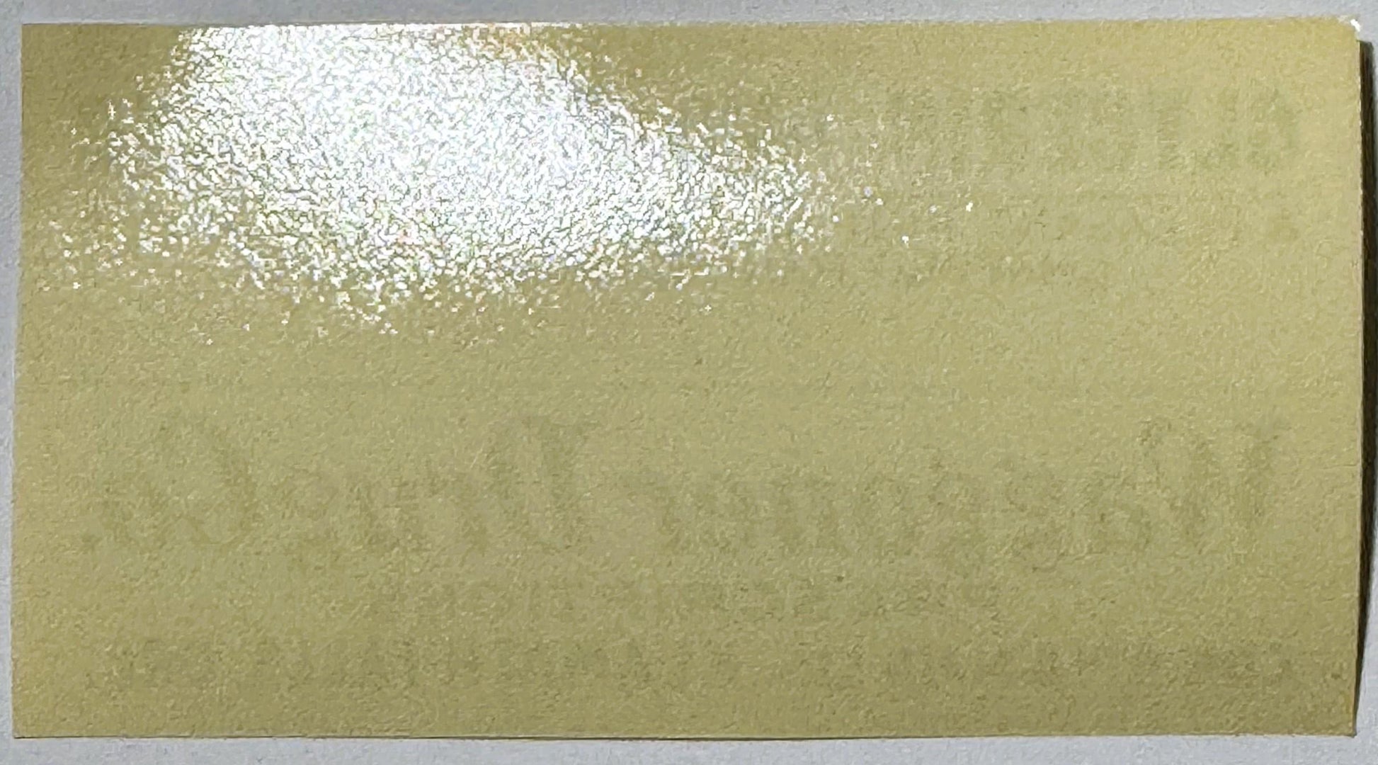 Vintage cream-colored label with white powder residue in upper left corner, blank surface visible against plain background
