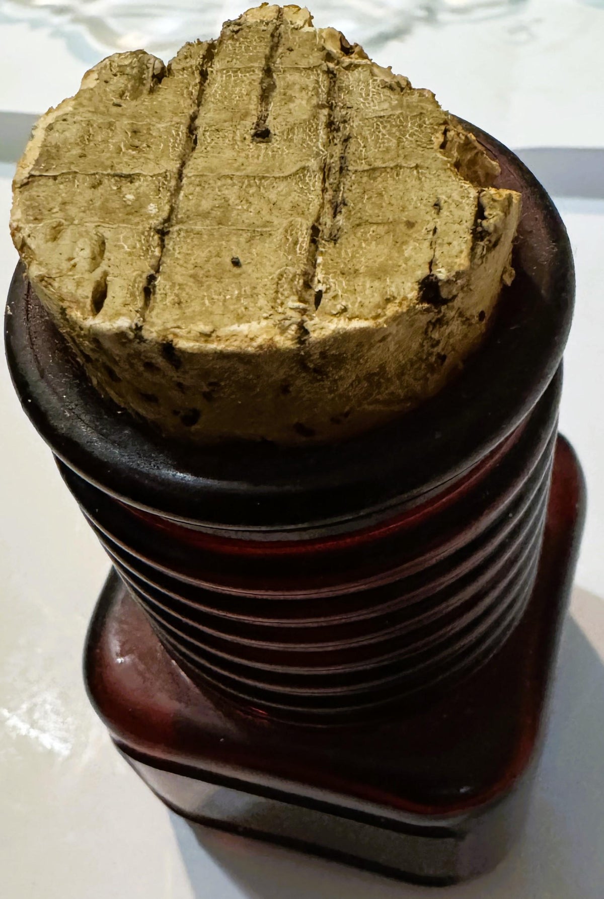 Close-up from a slightly higher angle of the cork stopper's worn, crumbling top and the ribbed glass neck beneath it.