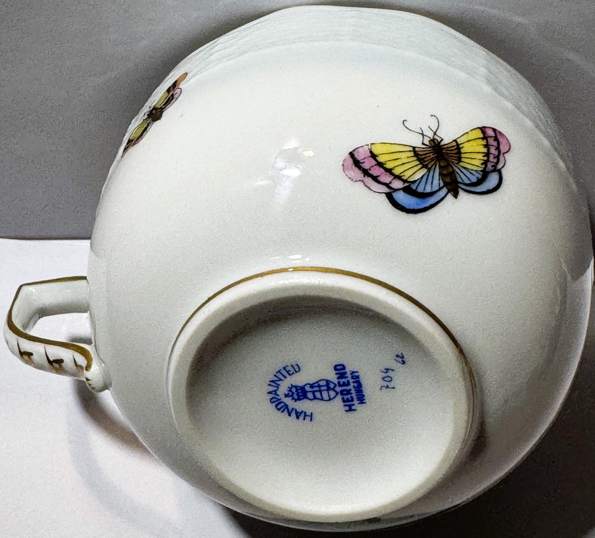 Vintage Herend porcelain teacup with colorful butterfly and bird motifs, gilt handle and rim, blue maker's mark visible on ba