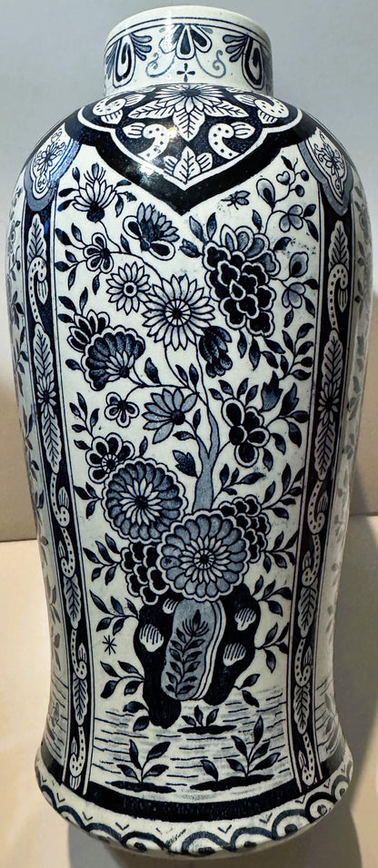 Tall cylindrical blue and white ceramic vase with floral motifs, decorative neck band, and ornamental base, displayed against