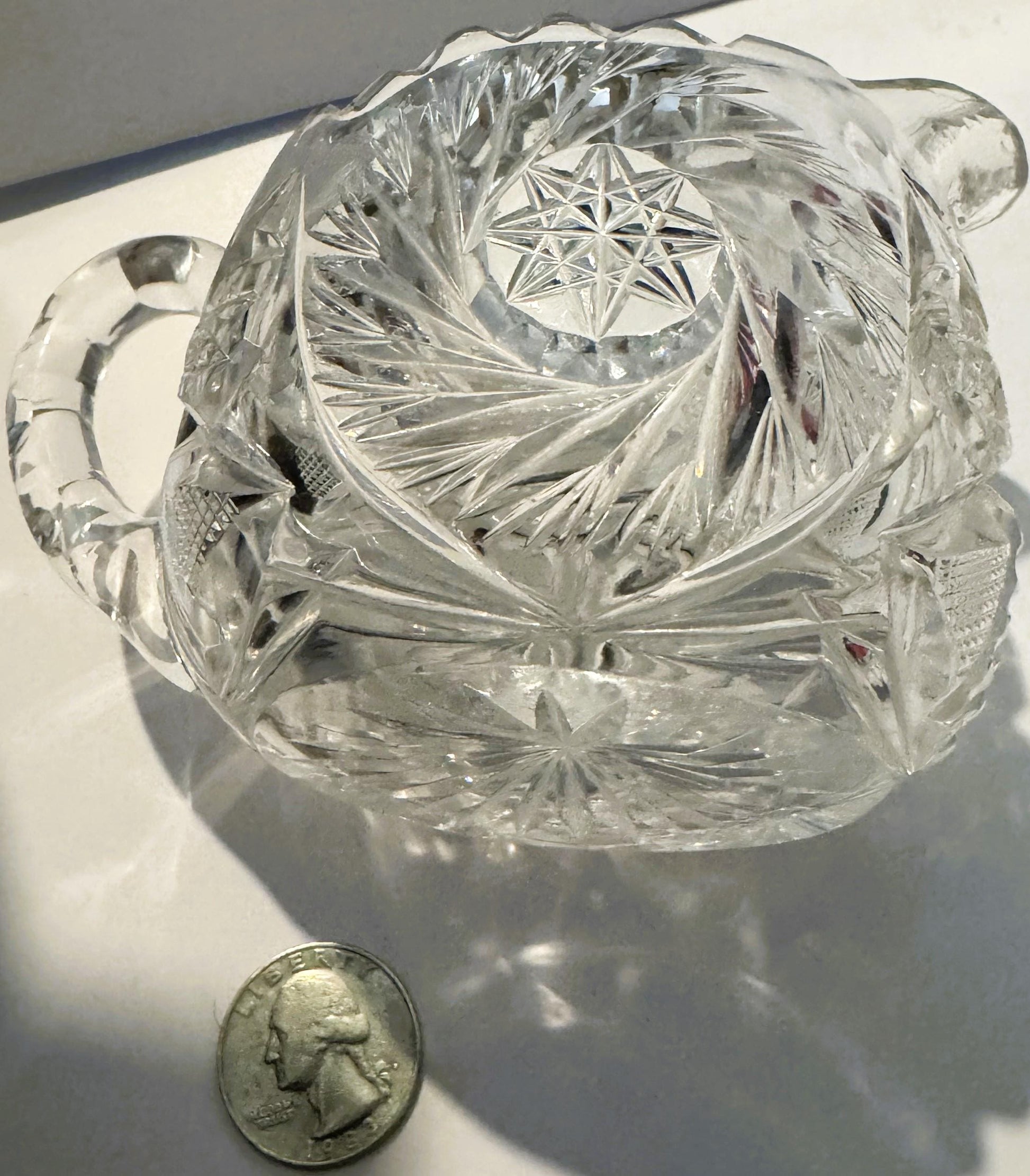 Clear cut glass creamer with pinwheel and hobstar patterns, shown at angle with quarter coin for scale