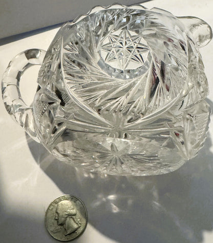 Clear cut glass creamer with pinwheel and hobstar patterns, shown at angle with quarter coin for scale
