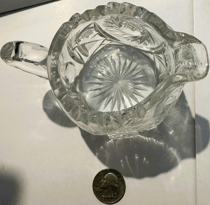 Clear glass creamer with pinwheel and hobstar cut patterns, shown from above with a quarter coin for scale