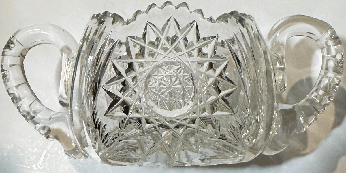 Antique cut glass two-handled sugar bowl with geometric star and fan patterns, photographed against white background
