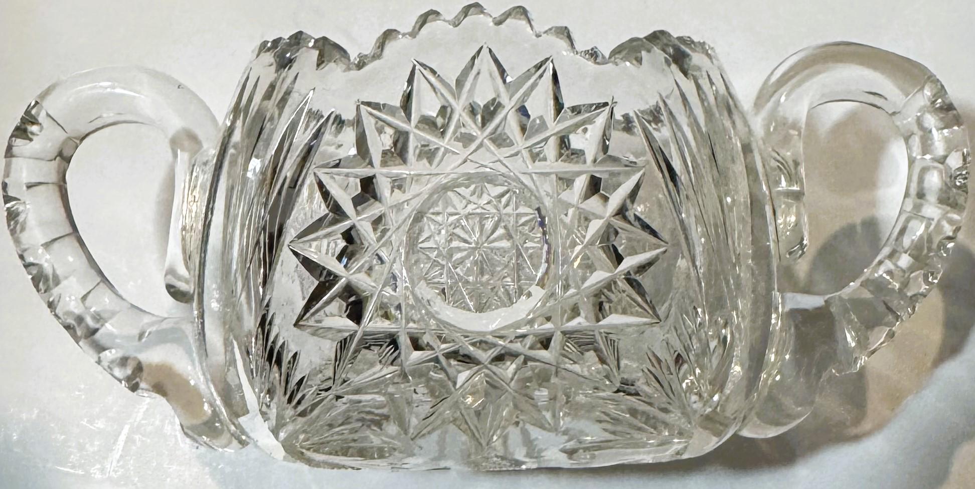 Antique cut glass two-handled sugar bowl with geometric star and fan patterns, photographed against white background