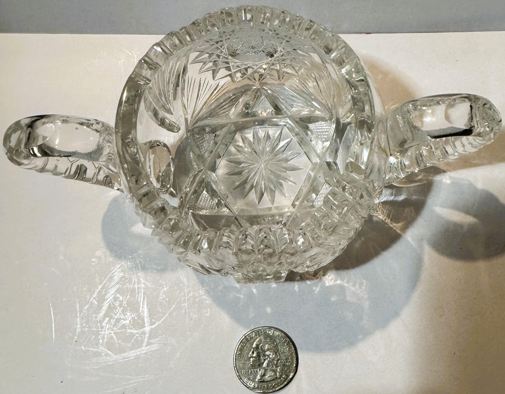 Antique cut glass two-handled sugar bowl with star and geometric patterns, shown from above with a quarter coin for scale