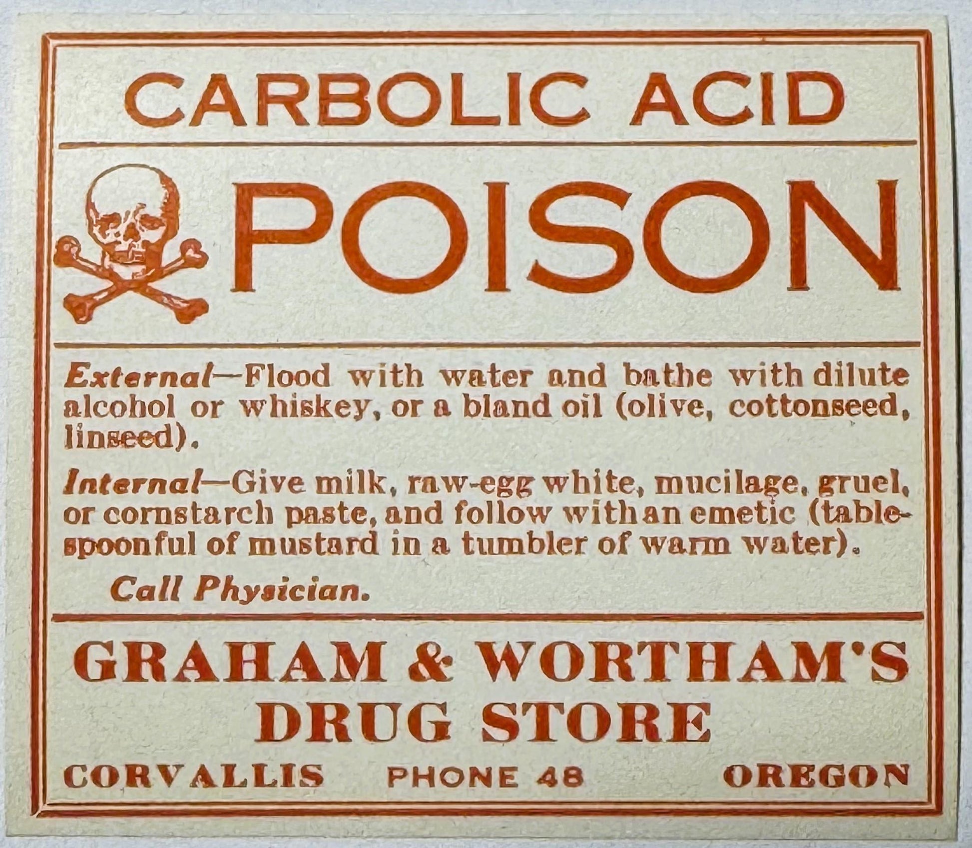 Vintage poison warning label with skull and crossbones, rust-red text on cream paper, listing carbolic acid antidote instruct