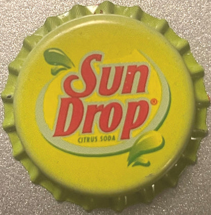 Yellow Sun Drop citrus soda bottle cap with red text and green leaf design, shown flat on textured surface