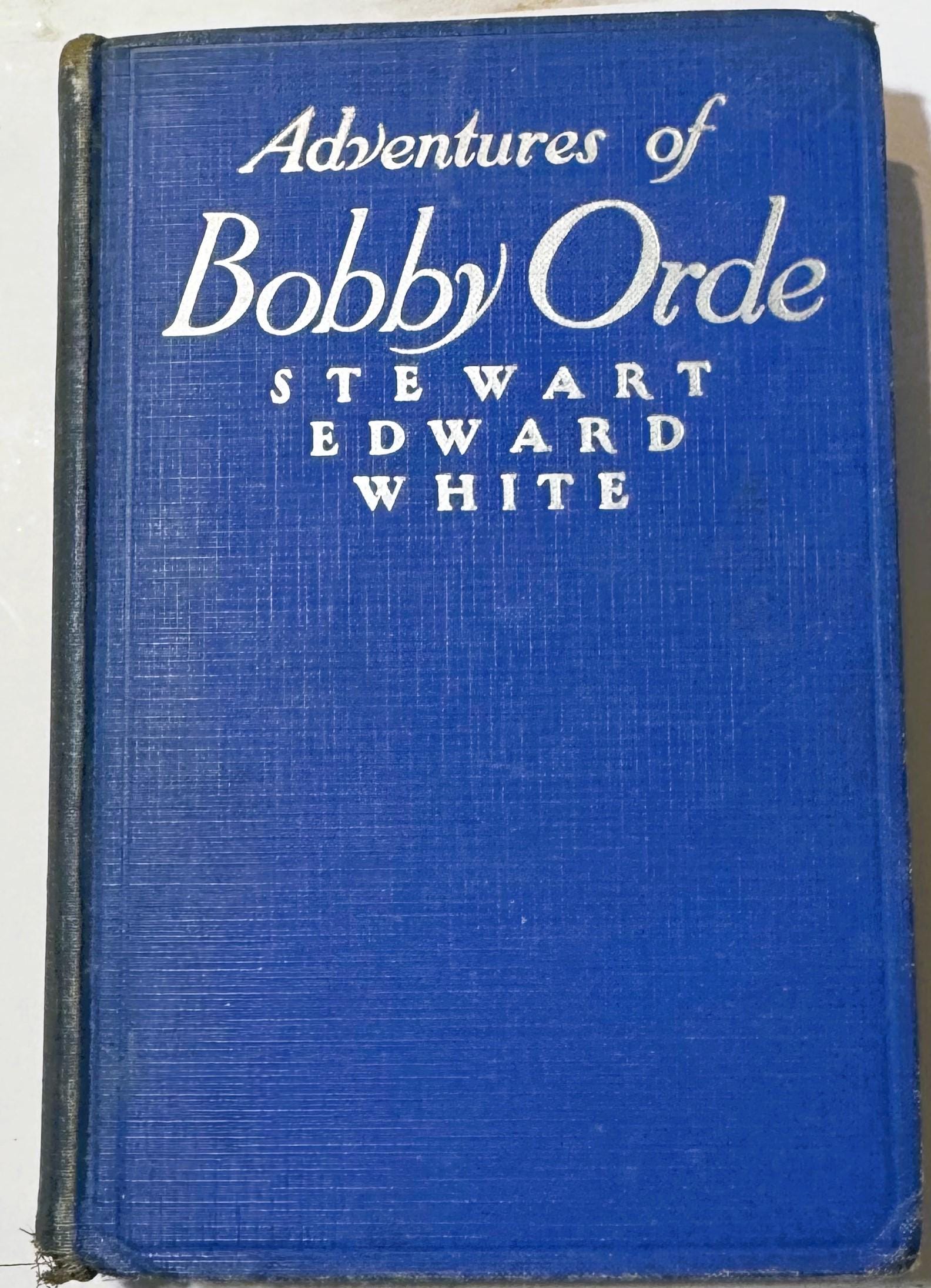 Blue cloth hardcover book with white serif title text reading "Adventures of Bobby Orde" and author "Stewart Edward White