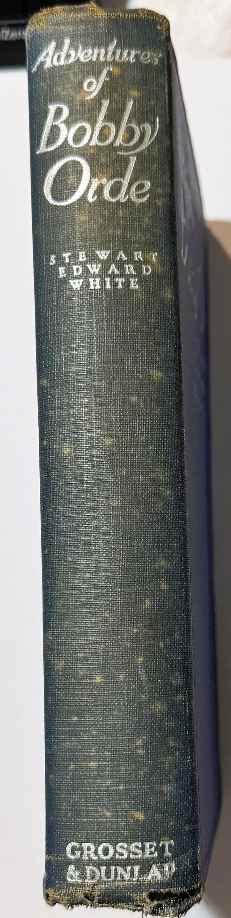 Spine of a dark green cloth hardcover book titled "Adventures of Bobby Orde" by Stewart Edward White, published by Grosset & 