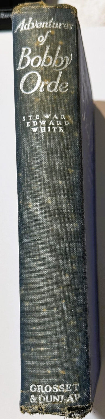 Spine of a dark green cloth hardcover book titled "Adventures of Bobby Orde" by Stewart Edward White, published by Grosset & 