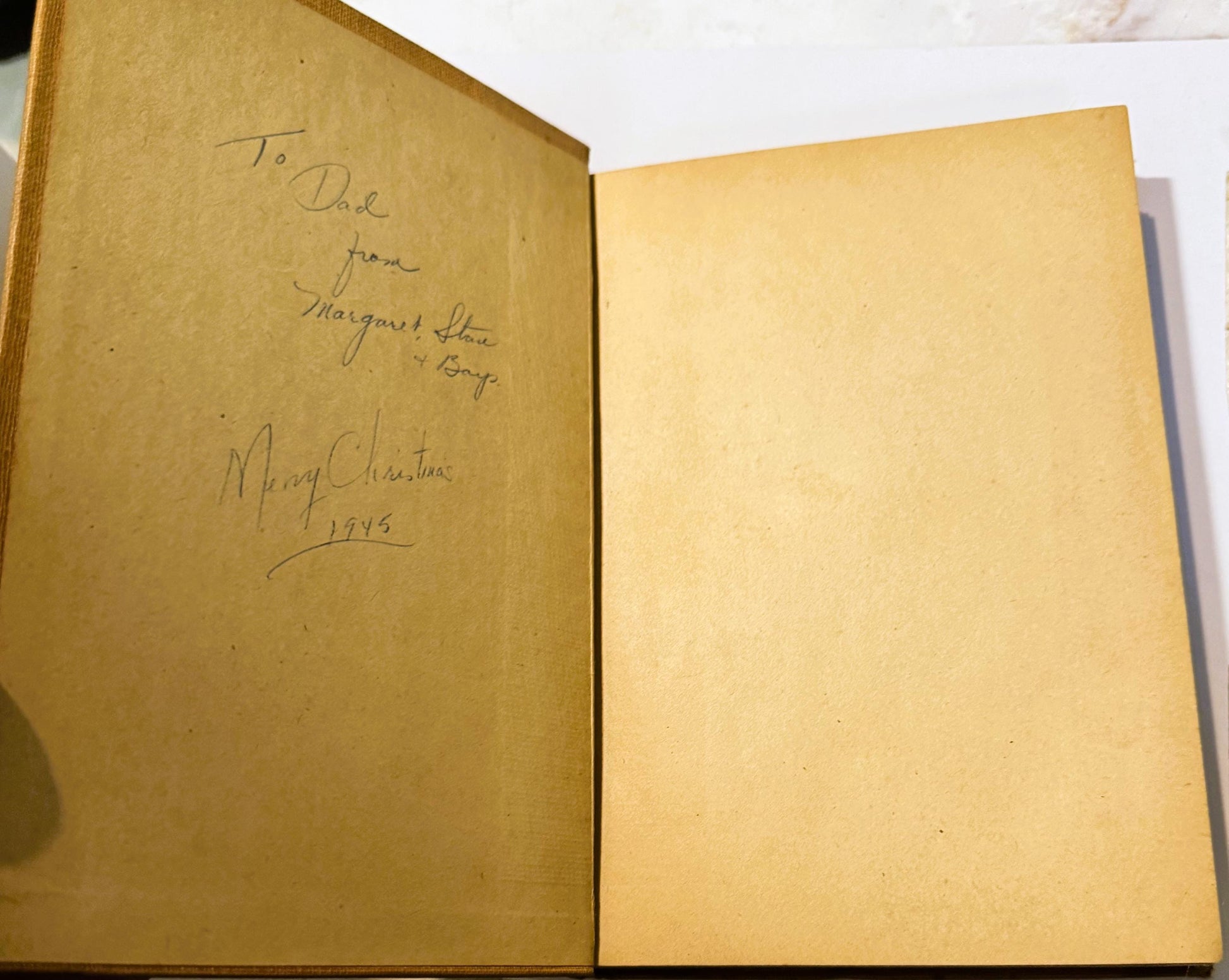 Open vintage book showing inside front cover with handwritten inscription dated 1945 and blank right page, cream-colored page