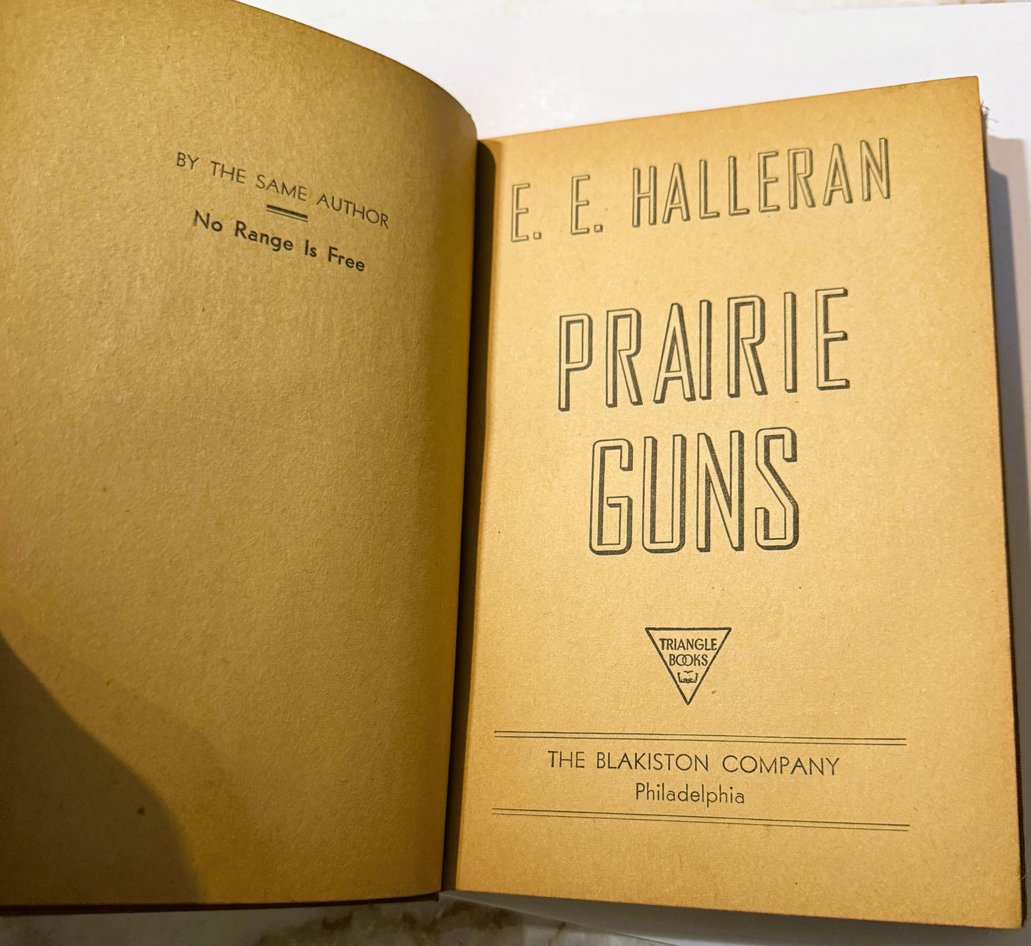 Open vintage book showing title page for "Prairie Guns" by E.E. Halleran, published by The Blakiston Company Philadelphia, wi