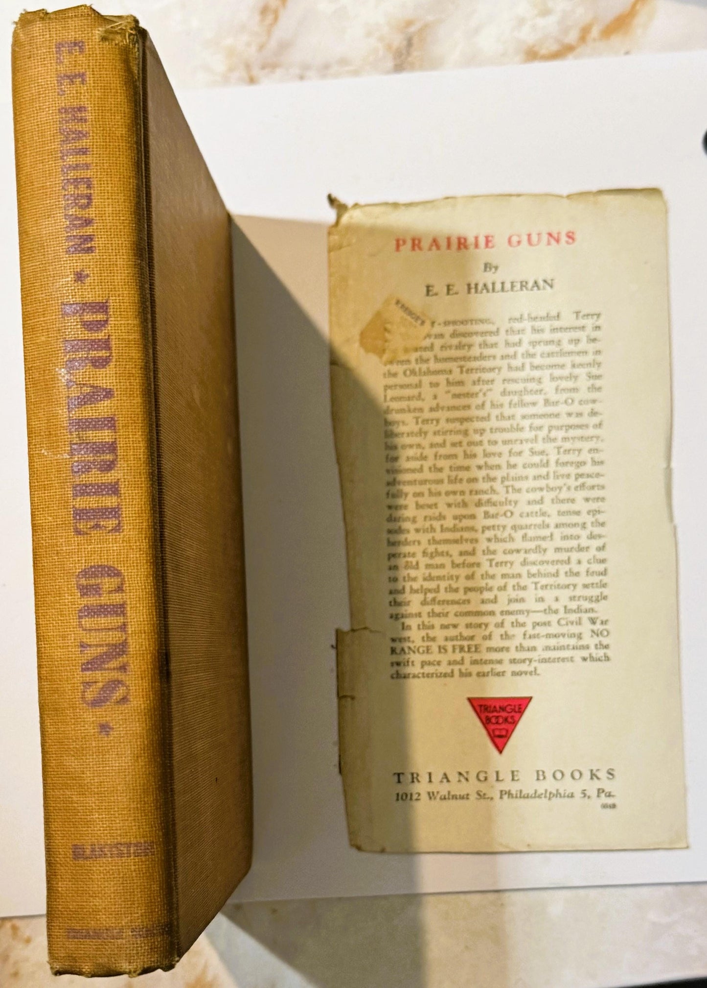 Open vintage hardcover book showing gold cloth spine and dust jacket for "Prairie Guns" by E.E. Halleran, published by Triang