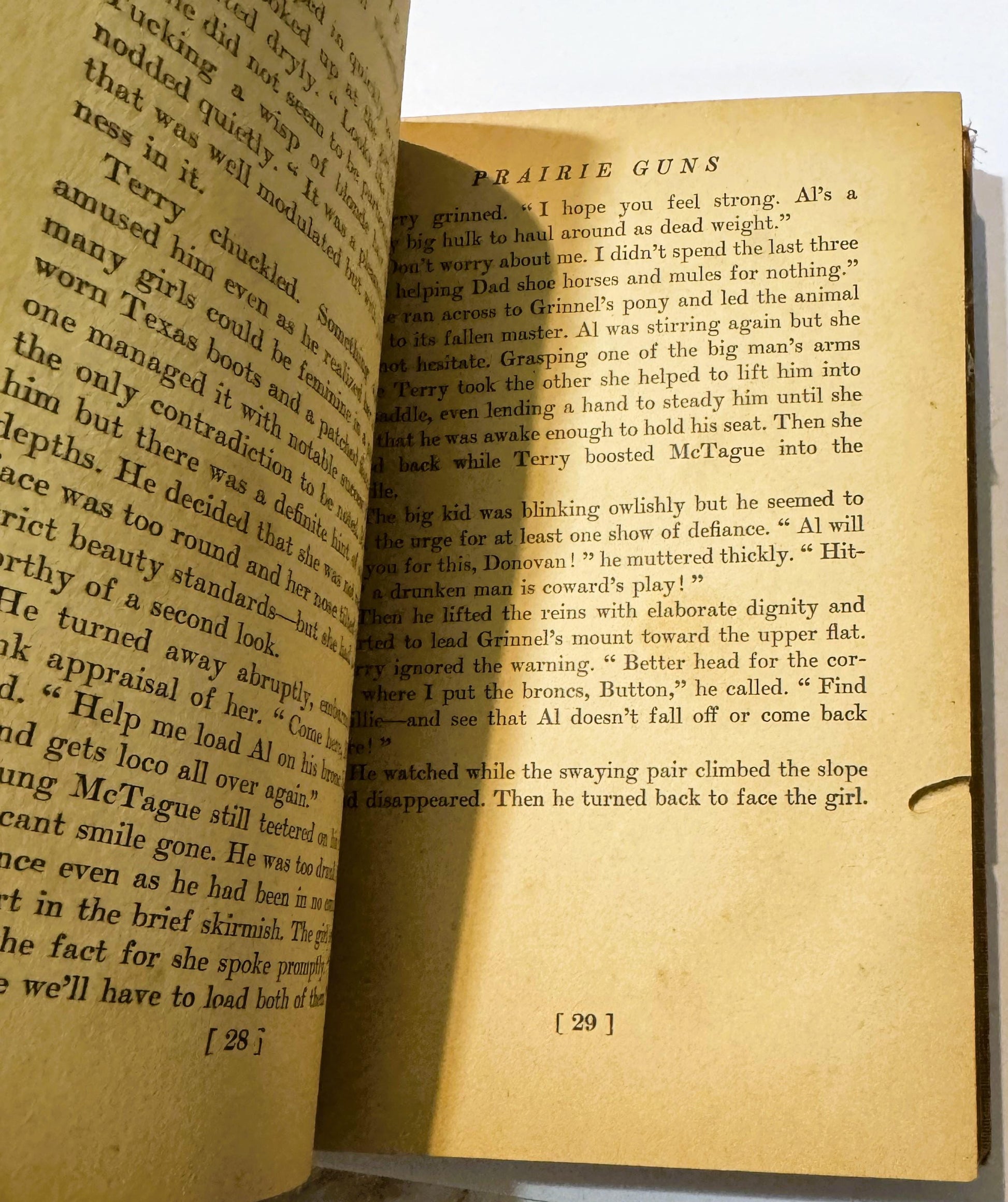 Open vintage book showing pages 28-29 of "Prairie Guns," yellowed pages with black text describing a scene with characters na