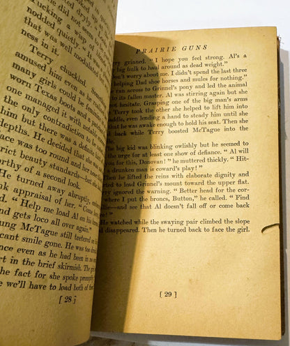 Open vintage book showing pages 28-29 of "Prairie Guns," yellowed pages with black text describing a scene with characters na