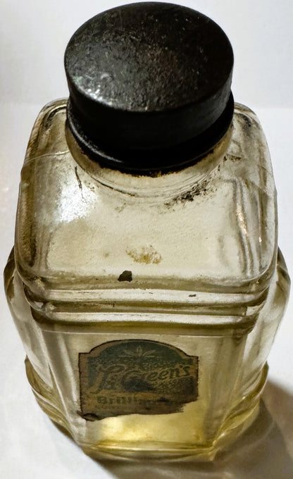 Vintage La Green's Brilliantine bottle with black cap, pale yellow liquid, and embossed label, viewed from above against whit