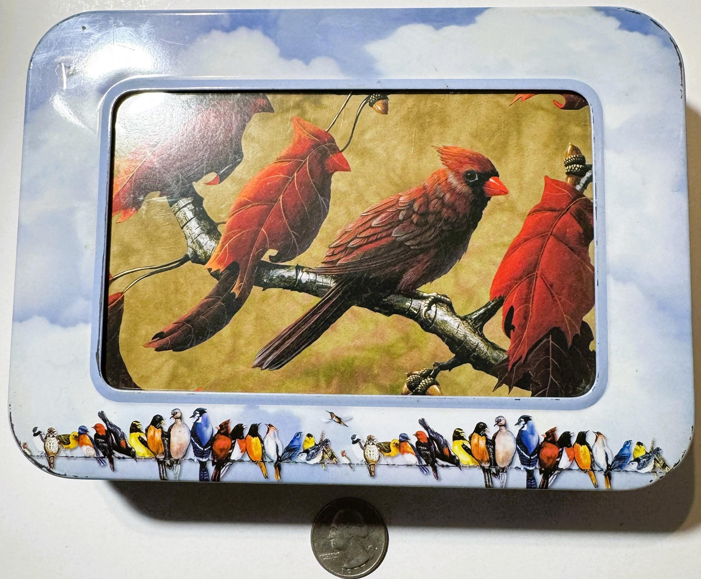 Vintage tin box with sky-blue lid featuring red cardinal birds on branch with autumn leaves, bordered by colorful songbirds; 