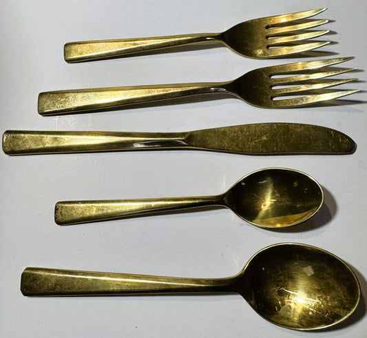 Five brass flatware pieces arranged in rows on white surface: two forks, knife, and two spoons with polished gold tone finish
