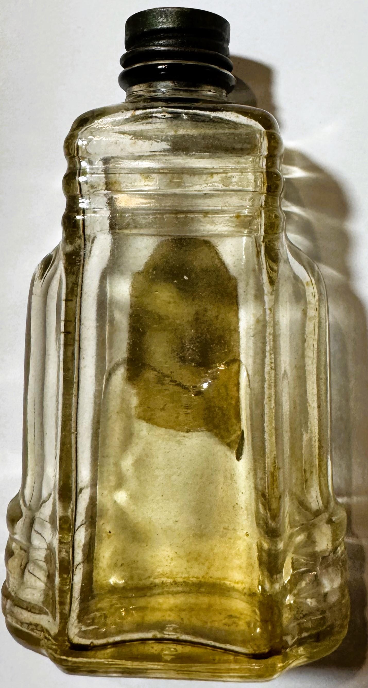 Vintage clear glass bottle with yellowish liquid and black screw cap, shot against white background with shadow visible