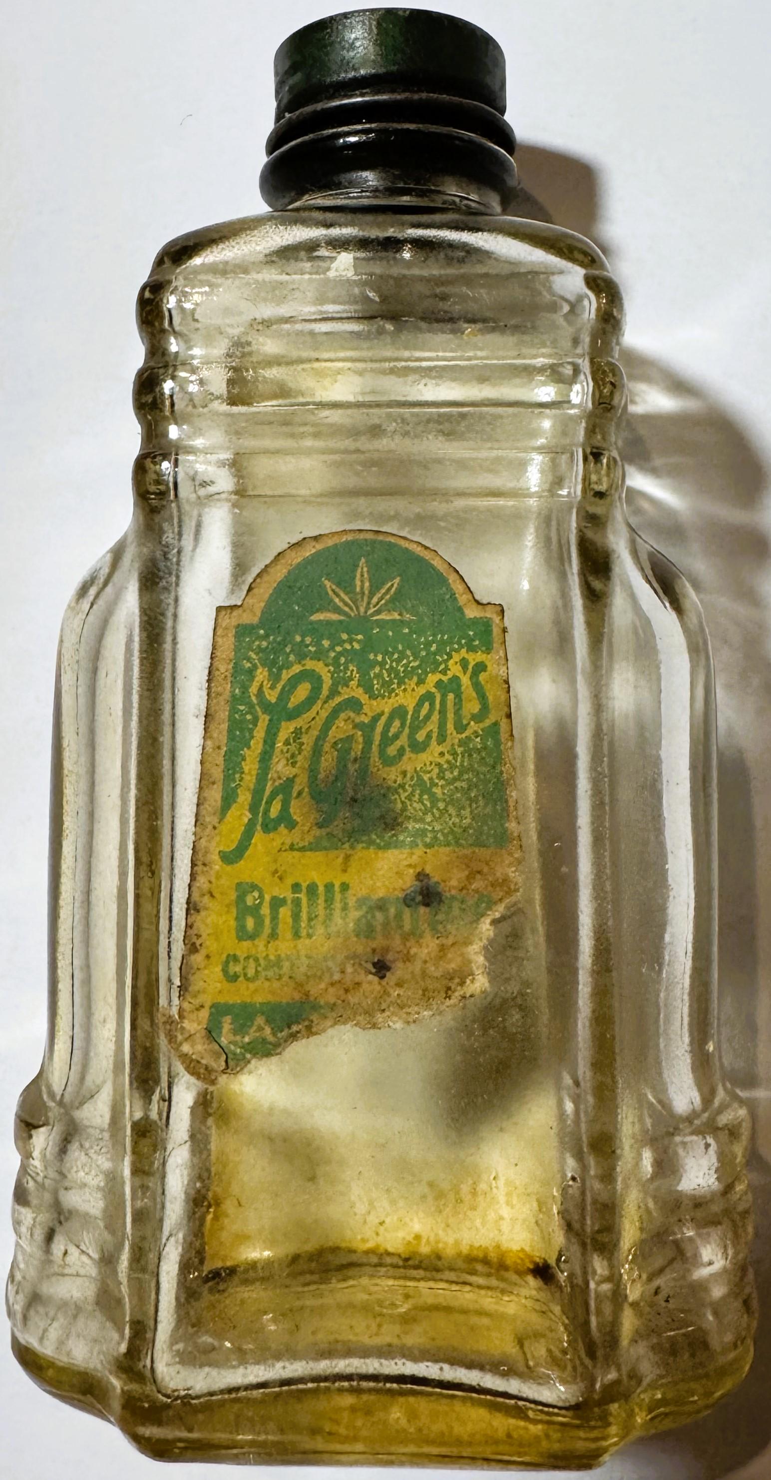 Vintage clear glass bottle with green and yellow label reading "La Green's Brilliantine," black metal cap, photographed again